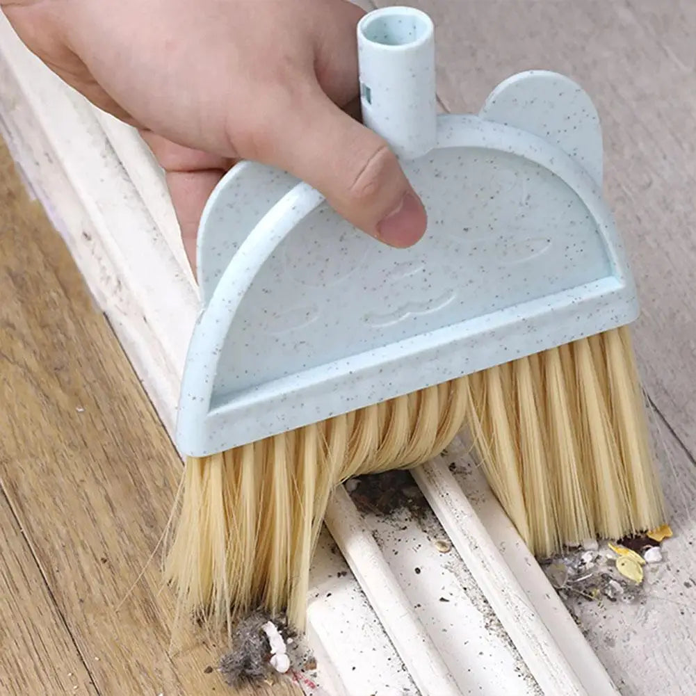 A hand is holding a light blue kids broom and dustpan set with adjustable mop on a wooden floor.