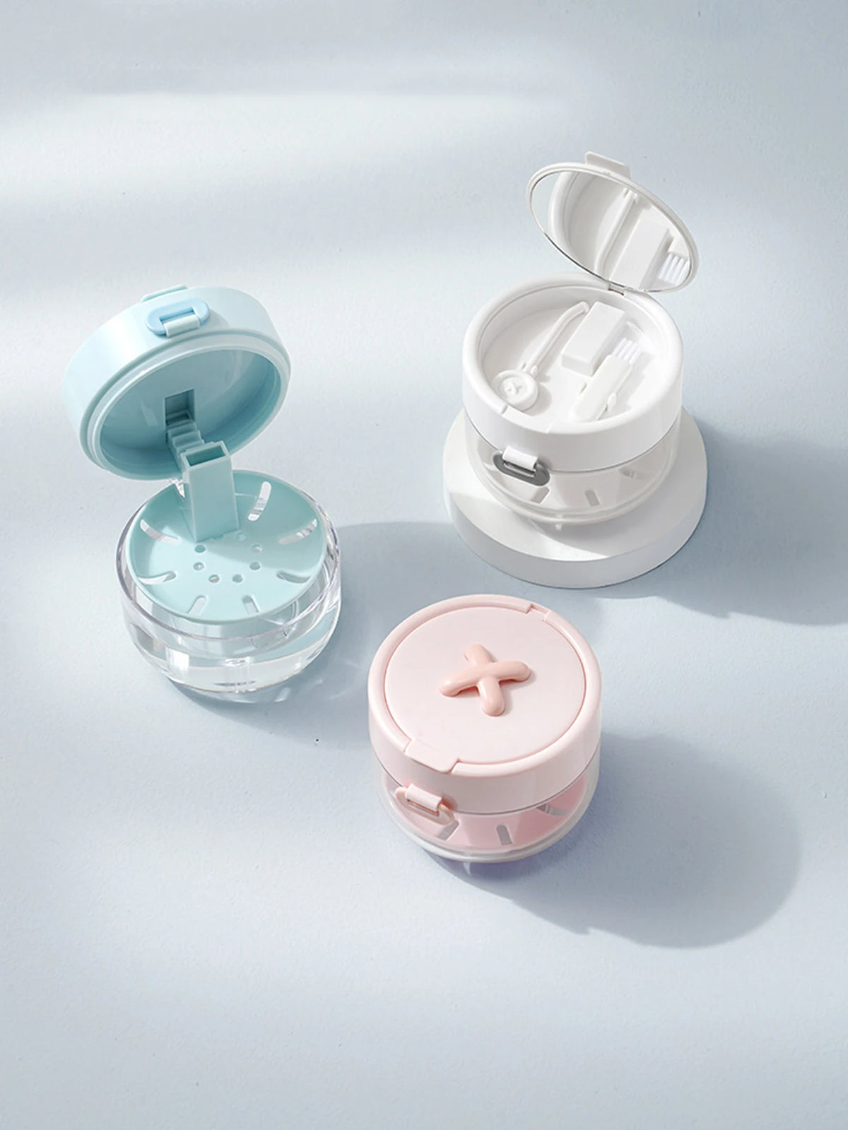 A portable denture case in light blue and white, showing an open lid and a separate pink storage container with a cleaning br