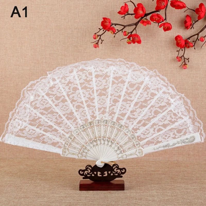 White lace folding fan with floral design displayed against a background of red blossoms.