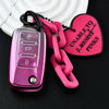 A pink soft TPU car key cover attached to a chain and a heart-shaped tag with text on a black background.