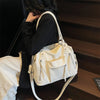 A woman holds a cream-colored soft leather plaid crossbody bag with a white strap against a dark background.