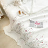 White quilted bedspread with delicate floral embroidery and a small plate of bread on a bed.