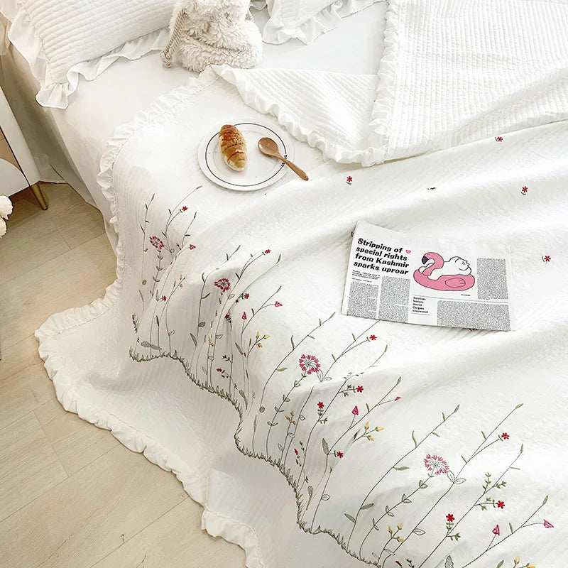 White quilted bedspread with delicate floral embroidery and a small plate of bread on a bed.