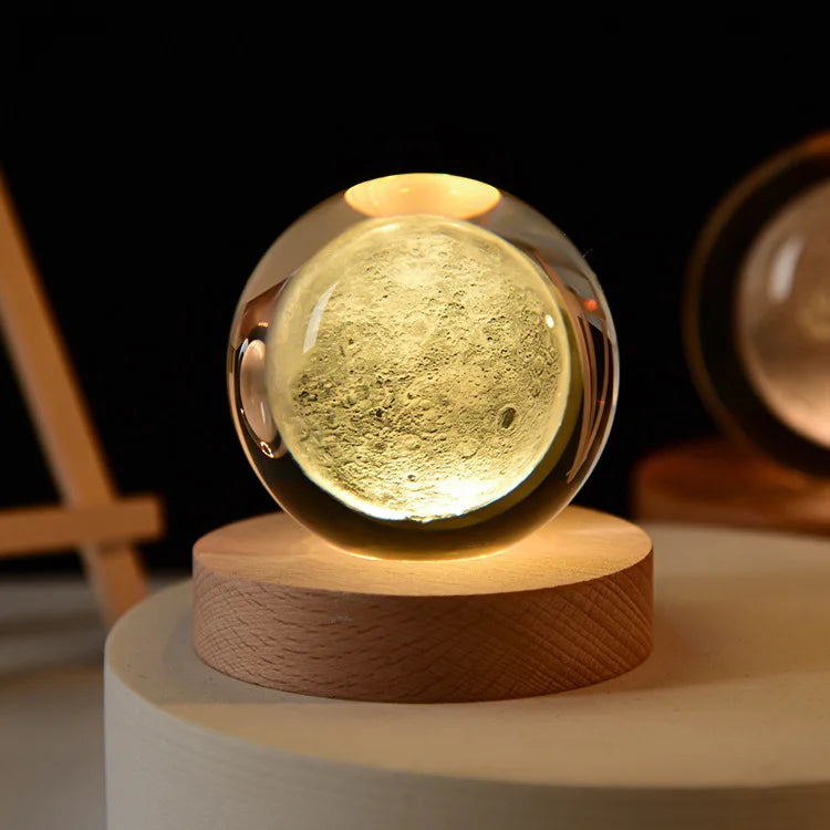 Laser engraved crystal ball night light with a golden glow resting on a wooden base.