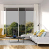 A modern living room interior showing a large glass door with privacy film, flanked by white curtains and a wooden floor.