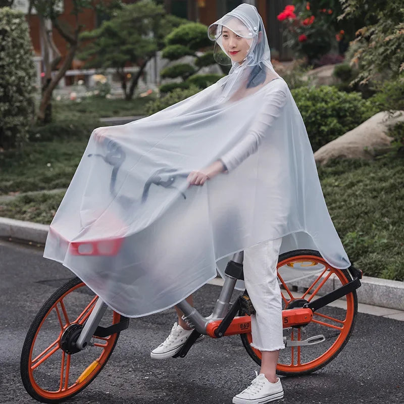 A woman wearing a transparent waterproof motorcycle rain poncho with a hood rides a bicycle on a street.