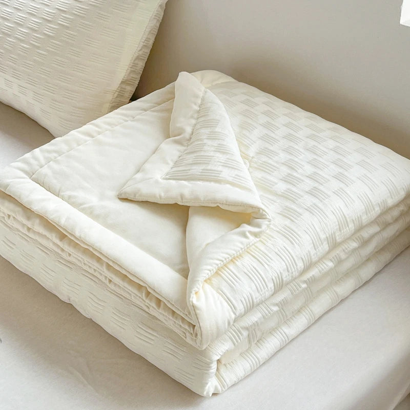A stack of white breathable waffle-weave summer quilts folded neatly on a bed.