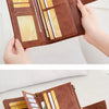A close-up display of a brown leather bifold wallet with multiple card slots and a strap, held by hands.