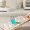 A wooden drawer mat with a floral pattern is shown under a glass of blue liquid.