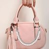 A hand holds a pink leather purse with a pearl and gold chain detail.