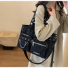 A black nylon shoulder bag with silver chain accents is worn by a person in a beige coat.