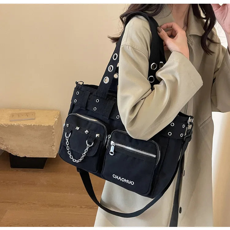 A black nylon shoulder bag with silver chain accents is worn by a person in a beige coat.