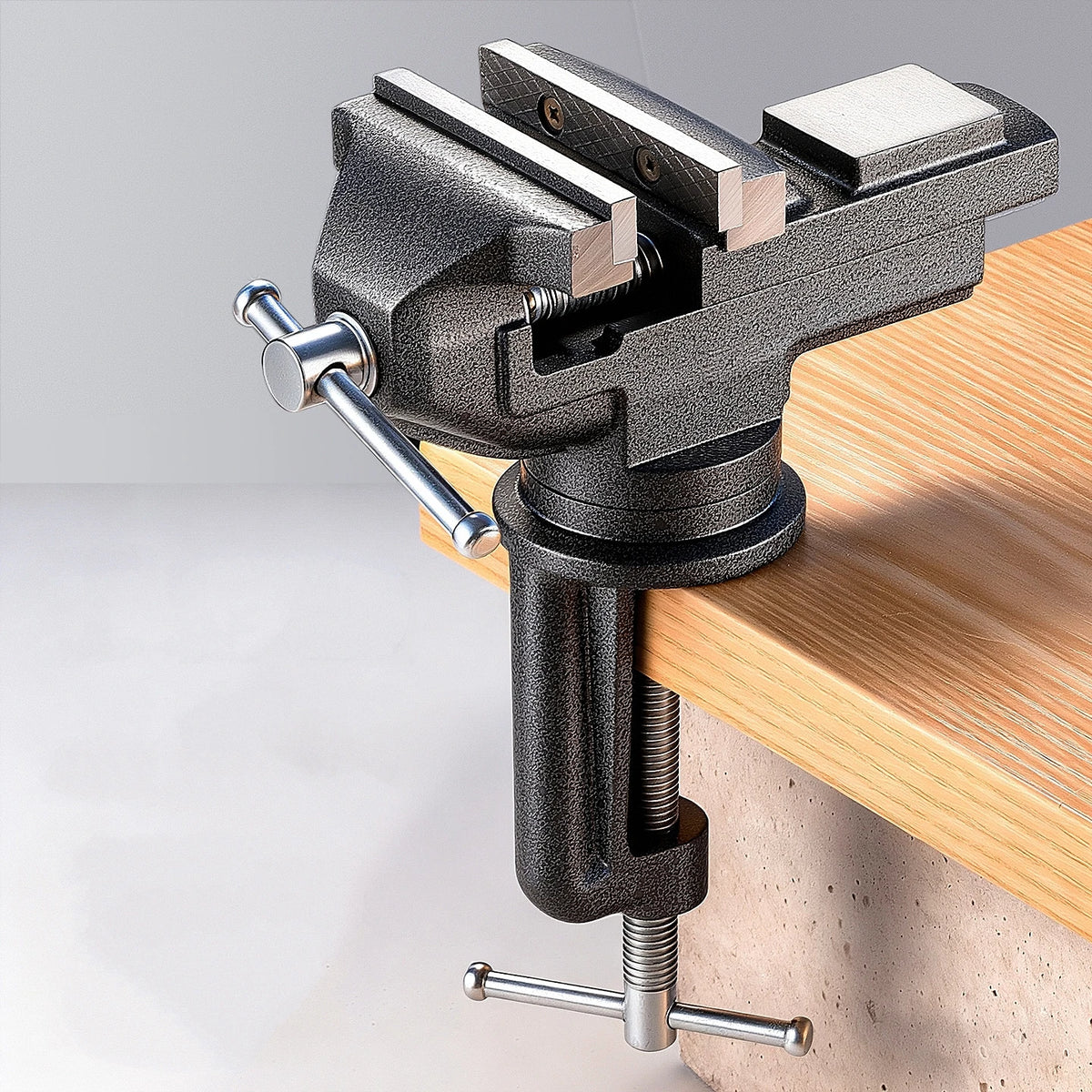 A black clamp-on table vise with a swivel mechanism is mounted on a wooden surface.