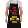 A man wearing a black chef apron with white text that reads Kiss the Cook and Bring him a beer