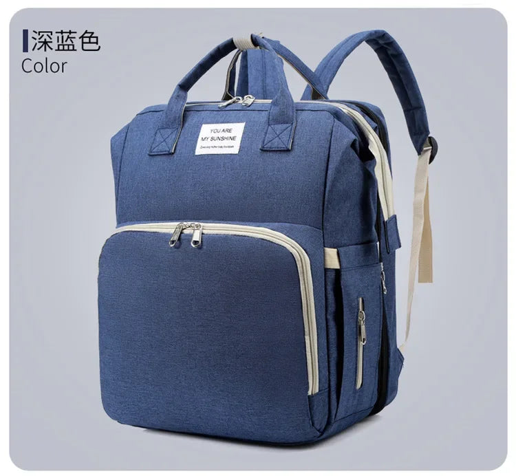A navy blue backpack diaper bag featuring a zippered compartment and a light beige changing mat.