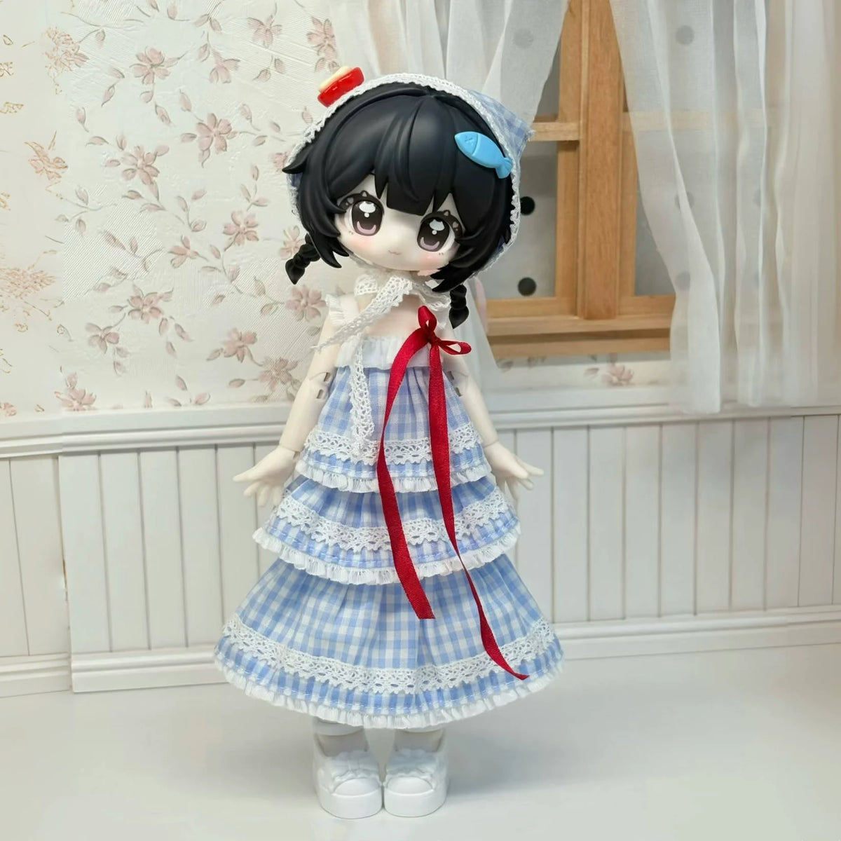 An articulated BJD collectible figurine with black hair, a white and blue checkered dress, and a red ribbon, standing in a li