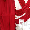 A close-up of rich red fabric draped in elegant folds against a white background with red accents and a white chair.