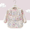 A light pink children's waterproof long sleeve feeding bib with a catch pocket, featuring a floral print.