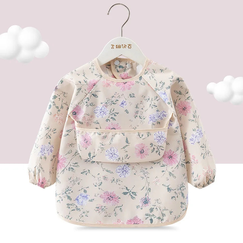A light pink children's waterproof long sleeve feeding bib with a catch pocket, featuring a floral print.