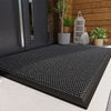 Black non-slip water-resistant doormat with a diamond mesh pattern placed on a light gray floor.