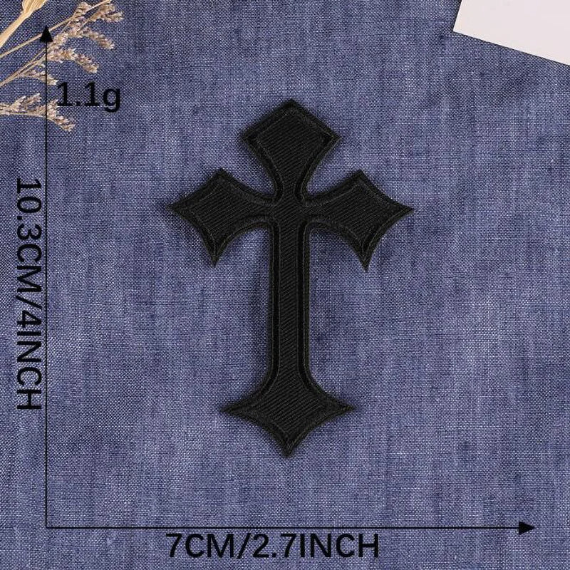 A black embroidered cross patch on a blue denim fabric background.