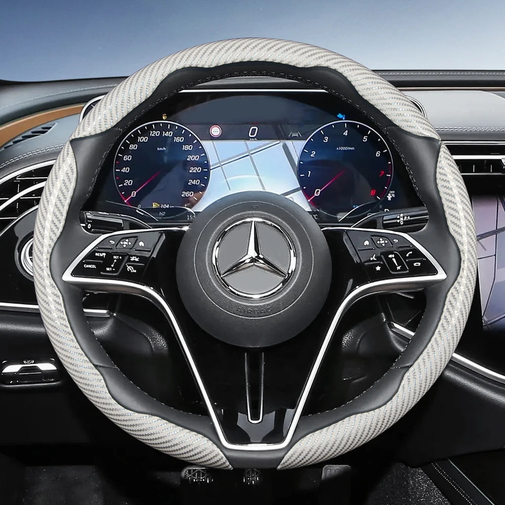 Close-up view of a black steering wheel with a carbon fiber texture cover and Mercedes-Benz instrument cluster.