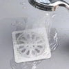 A white disposable drain hair catcher sticker is being rinsed under running water.