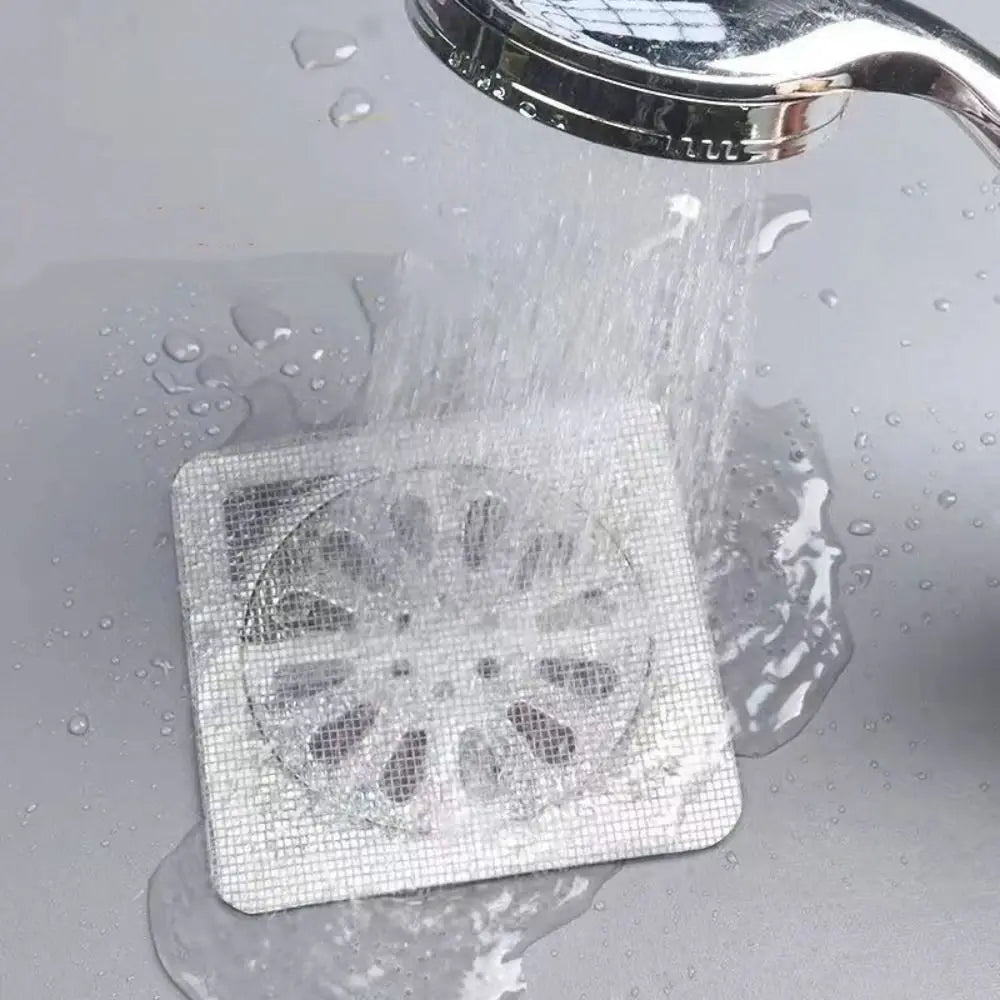 A white disposable drain hair catcher sticker is being rinsed under running water.