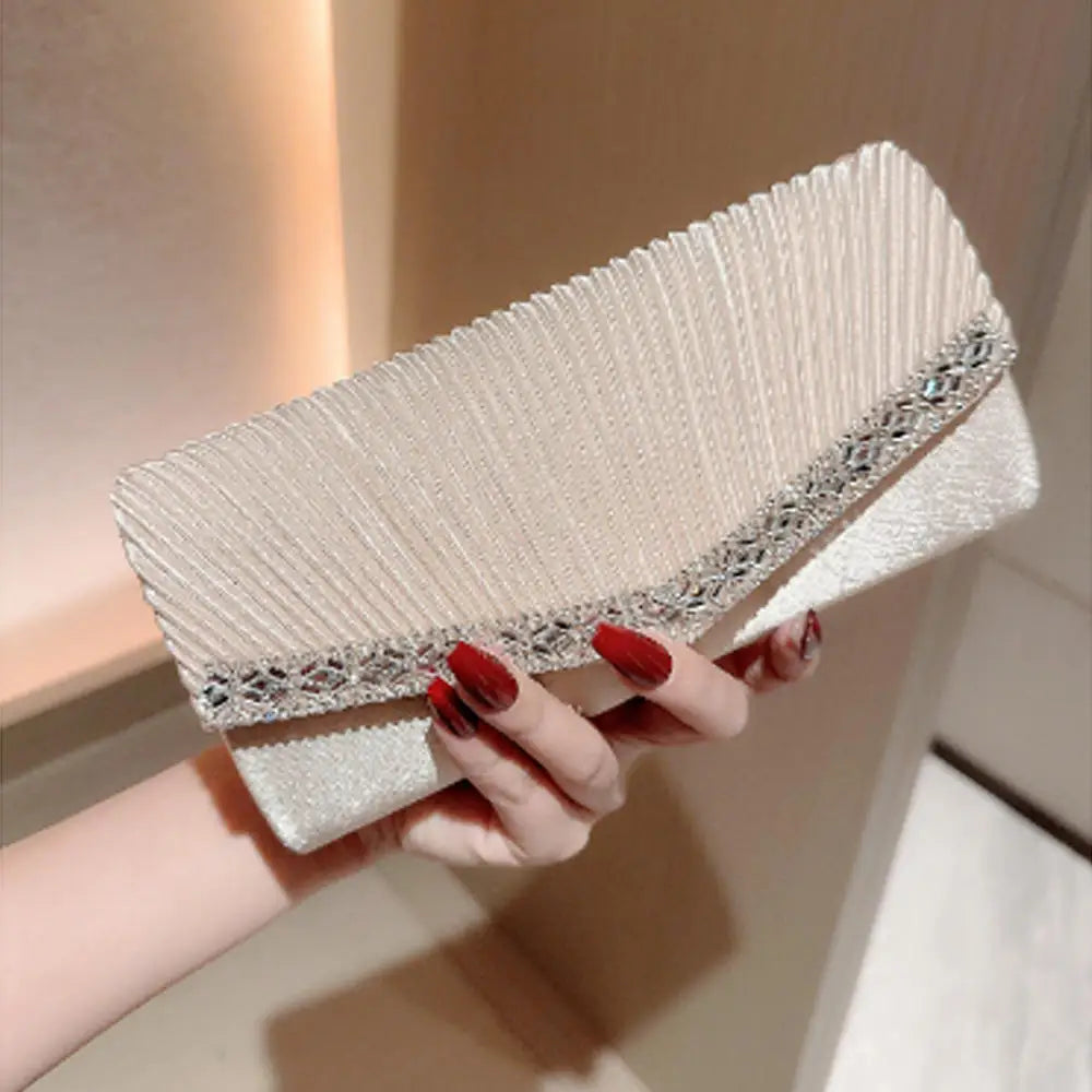 A hand holds an elegant patent leather clutch bag with a silver chain strap, featuring textured fabric and embellished edges.