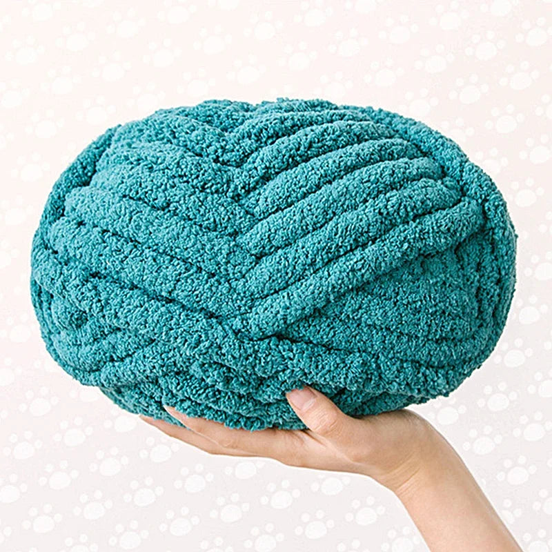 A hand is holding a teal chunky chenille yarn ball.