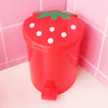 A red mini strawberry trash can with a green leaf lid sitting on a white surface.