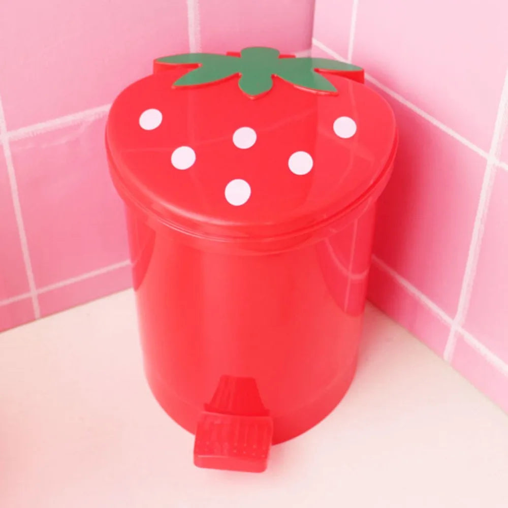 A red mini strawberry trash can with a green leaf lid sitting on a white surface.