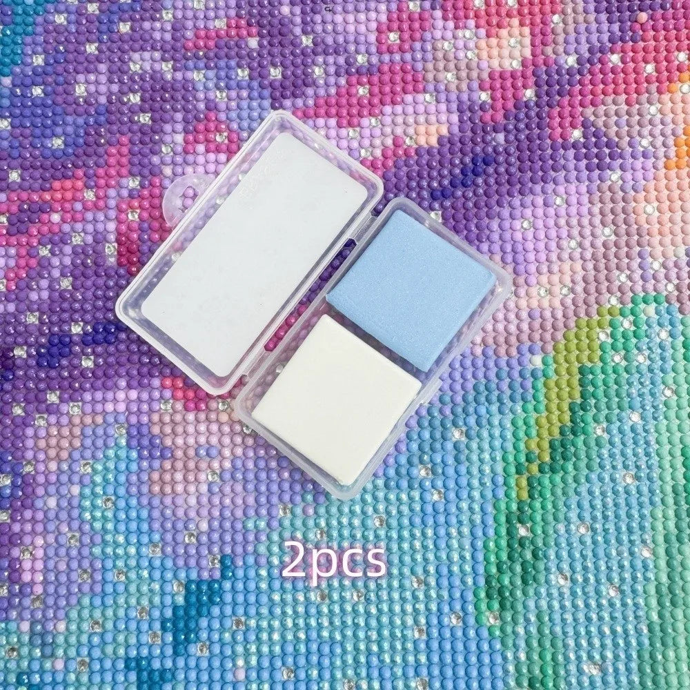 Two silicone diamond painting clay sticks in white and light blue set on a purple and green textured background