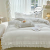 A white ruffled duvet cover set with matching pillowcases displayed on a bed in a bright room.