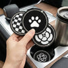 A hand holds three round coasters featuring a paw print, checkered pattern, and camellia design, resting in a car cup holder.