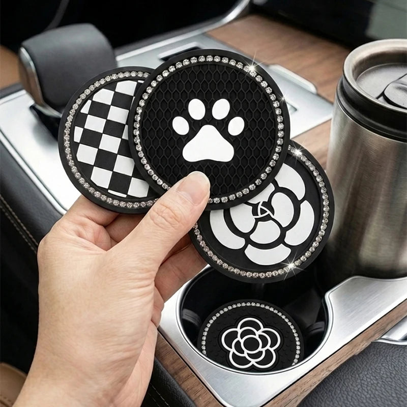 A hand holds three round coasters featuring a paw print, checkered pattern, and camellia design, resting in a car cup holder.