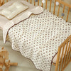A white cotton gauze baby swaddle blanket with a bear print pattern draped over a wooden crib.