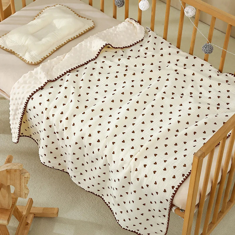 A white cotton gauze baby swaddle blanket with a bear print pattern draped over a wooden crib.