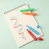 A set of twelve assorted fruit colored washable markers for kids displayed on a spiral notebook.