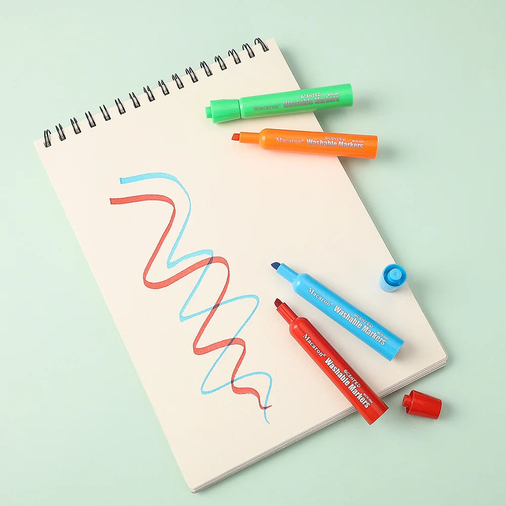 A set of twelve assorted fruit colored washable markers for kids displayed on a spiral notebook.