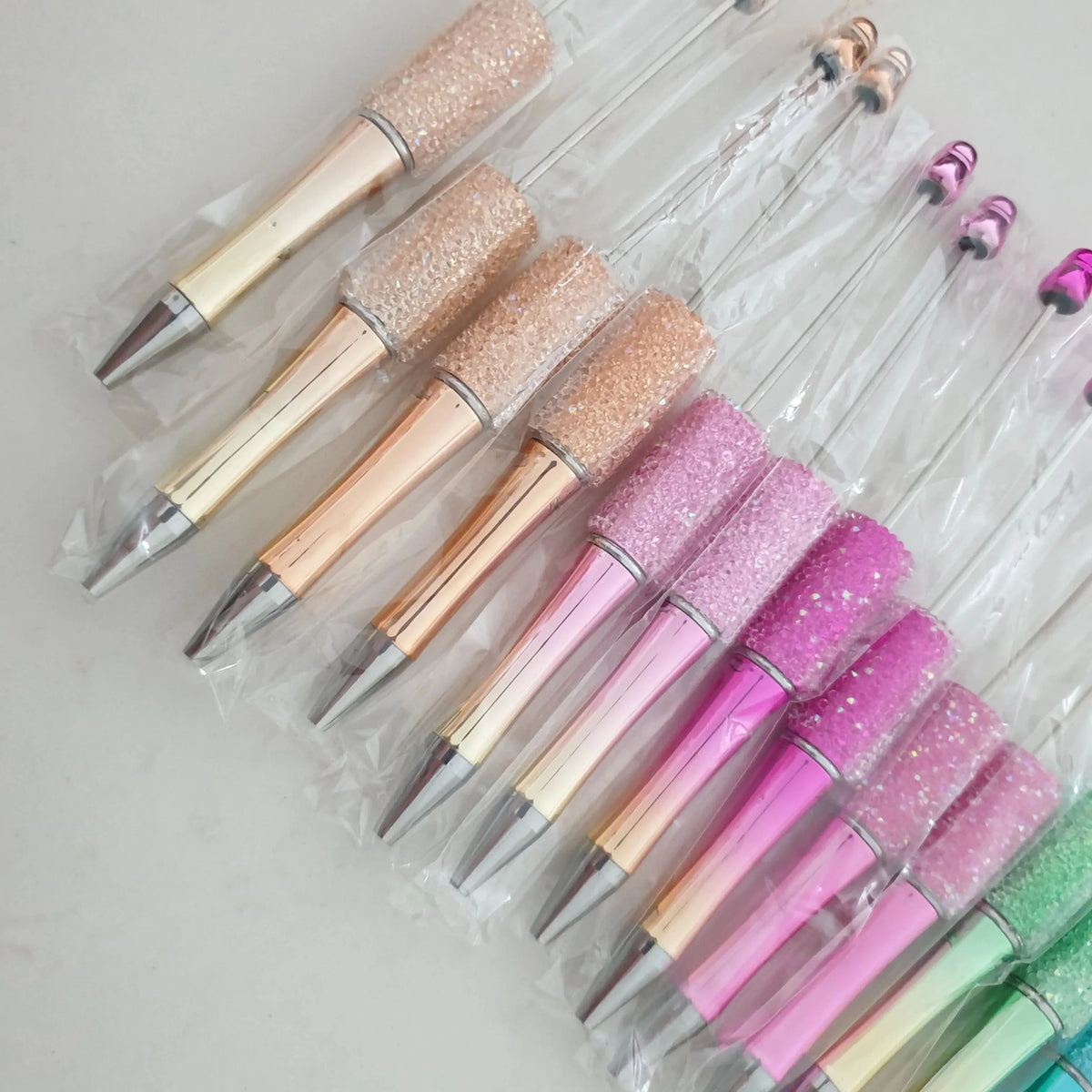 Une collection de trente stylos-plumes à bille perlés dans différentes nuances de rose et de vert sont présentés dans un emba