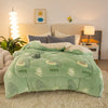 A light green plush throw blanket with leaf and oval patterns is displayed on a bed in a bright room.
