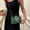 A woman holds a green rhinestone evening clutch with a gold chain strap against a black dress.