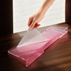 A hand places a pink acrylic ergonomic keyboard riser onto a wooden desk surface.