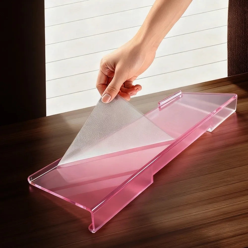 A hand places a pink acrylic ergonomic keyboard riser onto a wooden desk surface.