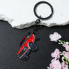 A red Ford Bronco zinc alloy keychain attached to a black ring, resting on a dark surface next to pink flowers.