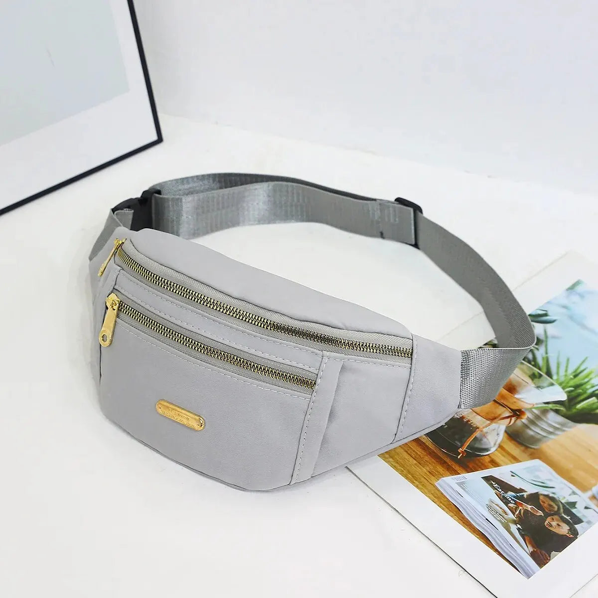 Graue Damen-Sport-Geldertasche mit Reißverschluss und goldenem Akzent auf weißem Untergrund.