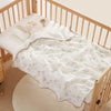 A white cotton gauze baby swaddle blanket with a bear print is laid on a wooden crib railing.