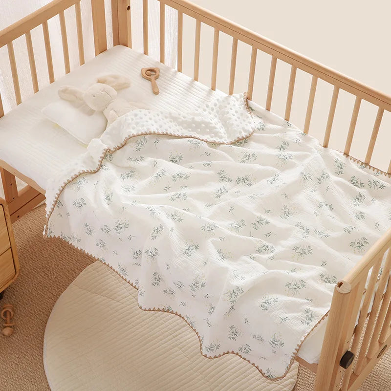 A white cotton gauze baby swaddle blanket with a bear print is laid on a wooden crib railing.