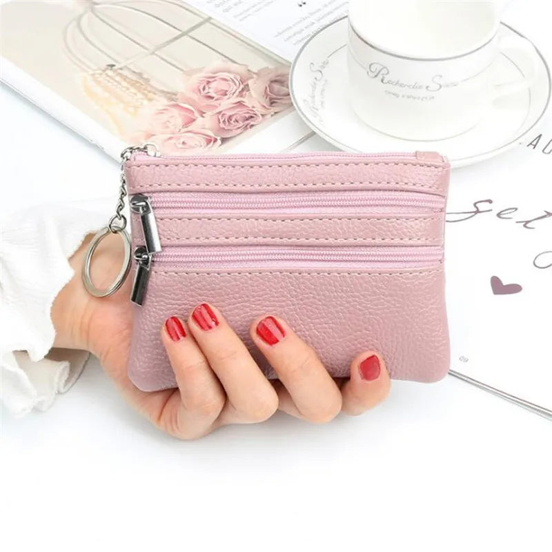 A pink PU leather compact two-zip coin purse is held in a woman's hand next to a white cup and some paper.